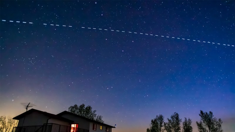 A line of bright spots representing satellites are seen in the night sky above a home